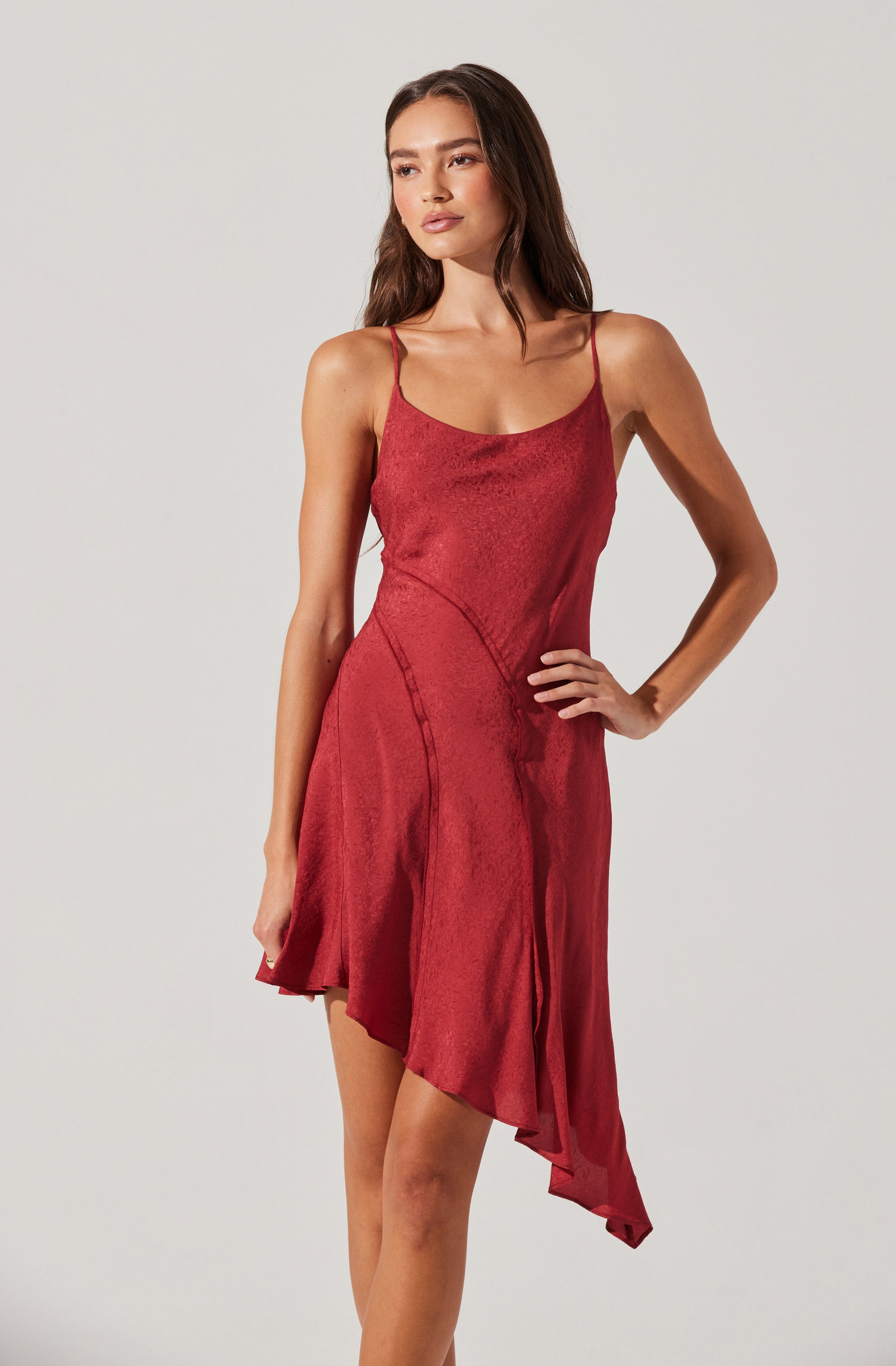 A woman is wearing a sleeveless, red, satin slip dress with thin spaghetti straps. The dress has a fitted bodice and a flowing, asymmetrical hemline.