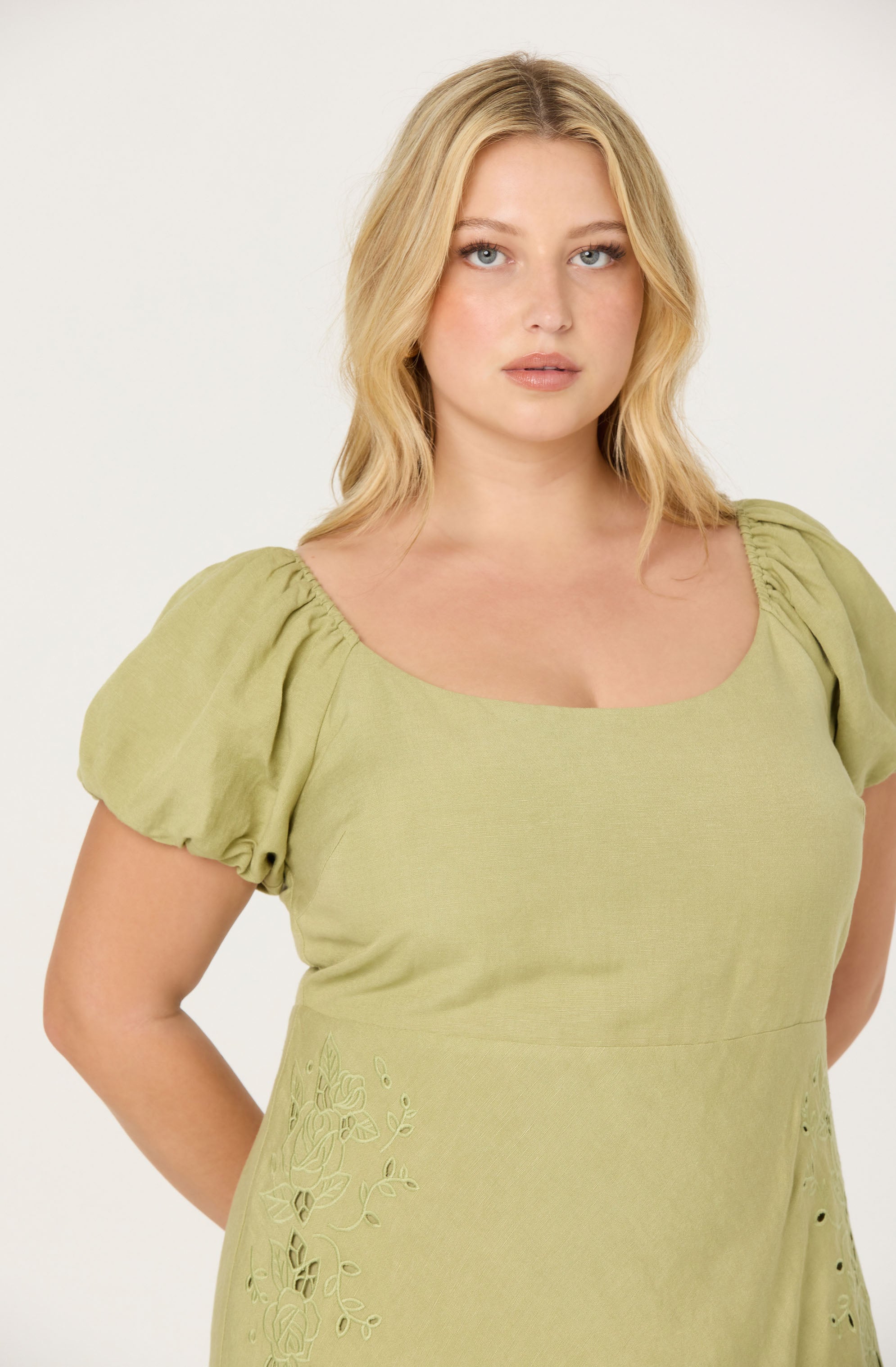 A woman wearing a light green dress with puffed short sleeves and embroidered floral details on the side.