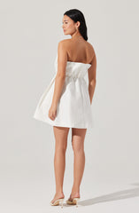 A woman is wearing a strapless white mini dress with a gathered waist. She has on beige high-heeled shoes with a pointed toe and stiletto heel. The dress appears to be made of a light, structured fabric.