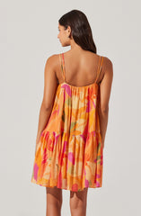 A woman is wearing a sleeveless dress with thin, adjustable spaghetti straps. The dress features a loose, flowing fit with a tiered design and a vibrant, abstract floral pattern in shades of orange, pink, yellow, and green.