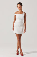A woman is wearing a white, off-the-shoulder, above-the-knee dress with short sleeves that feature tied bows. She is also wearing red high-heeled sandals.