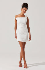 A woman is wearing a short, white, off-the-shoulder dress with tied bows on the shoulder straps. She has paired the dress with red high-heeled sandals.