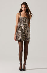 A woman is wearing a sleeveless, fitted dress with a square neckline and an all-over leopard print pattern. The dress has a slightly flared skirt that ends above the knees. She is also wearing sheer black tights and black high-heeled shoes with ankle straps.