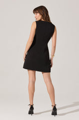 A woman is wearing a sleeveless, knee-length black dress with a fitted silhouette. The dress has a simple, classic design with no visible patterns or embellishments. She is also wearing a pair of black high-heeled shoes with ankle straps. Additionally, she has a gold bracelet on her left wrist.