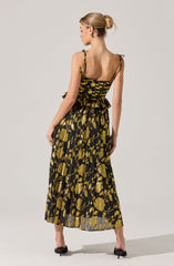 A woman is wearing a sleeveless dress with adjustable shoulder ties. The dress features a fitted bodice with a flared, ruffled waist. The fabric has a black base with a gold floral pattern throughout, and the skirt is long and flowing, reaching her ankles. She is also wearing black open-toe heels.