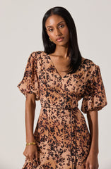 A woman is wearing a dress with a leopard print pattern. The dress has a V-neckline, short puffed sleeves, and a fitted waist. The fabric features tan and black spotted design, resembling animal print.