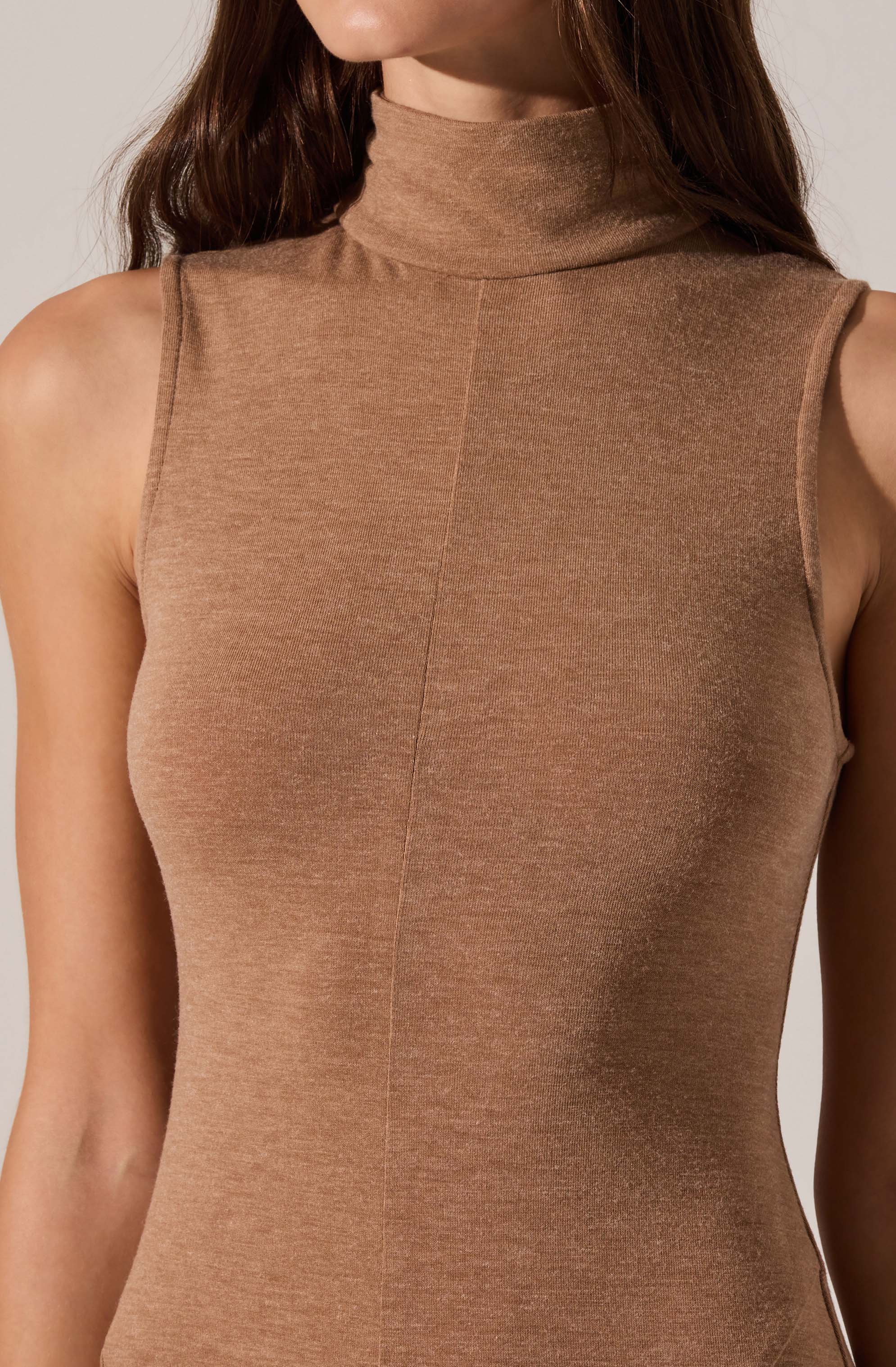 A sleeveless, form-fitting top with a high turtleneck collar in a light brown or camel color. The fabric appears smooth and slightly stretchy, with visible seam lines running vertically down the front. The armholes are slightly widened, and the top has no visible embellishments or patterns.