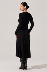 A woman is wearing a fitted, long-sleeve, ribbed black sweater paired with a matching ribbed black midi skirt. She is also wearing tall black leather boots with high heels. The outfit appears elegant and monochromatic.