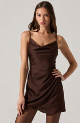 A woman wearing a sleeveless, dark brown satin dress with thin spaghetti straps. The dress features a cowl neckline and a draped, slightly asymmetrical hem.