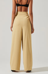 A woman is wearing high-waisted, wide-leg beige trousers with a smooth waistband, paired with a black bralette top with thin straps. The trousers have a tailored fit with subtle pleats near the waist, creating a flowy silhouette.