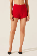 A person is wearing high-waisted, red shorts made of a textured, fuzzy fabric. They are also wearing black shoes with a bow detail on the front.