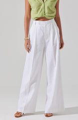A person is wearing a sleeveless, light green, cropped blouse with a V-neck and front pleats. They are also wearing high-waisted, wide-leg white linen pants with pleats near the waistband. The individual has gold bracelets and rings on their left hand and is wearing open-toed tan sandals.