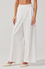 A person is wearing high-waisted, wide-leg white trousers with a tailored fit. The trousers feature pleats at the waistband and belt loops. The individual is also wearing pointed-toe beige high heels.