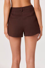 The image shows a person wearing high-waisted, tailored shorts made of a dark brown fabric. The shorts feature belt loops, two horizontal back pockets, and a clean, structured design with no visible embellishments. The person's upper body and face are not shown.
