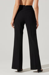 The image shows a person wearing high-waisted, wide-leg black trousers. The trousers have a tailored fit with a smooth front, belt loops, and two back pockets. The fabric appears to be structured and slightly shiny. The person is barefoot, with their upper body bare, revealing their back and arms.