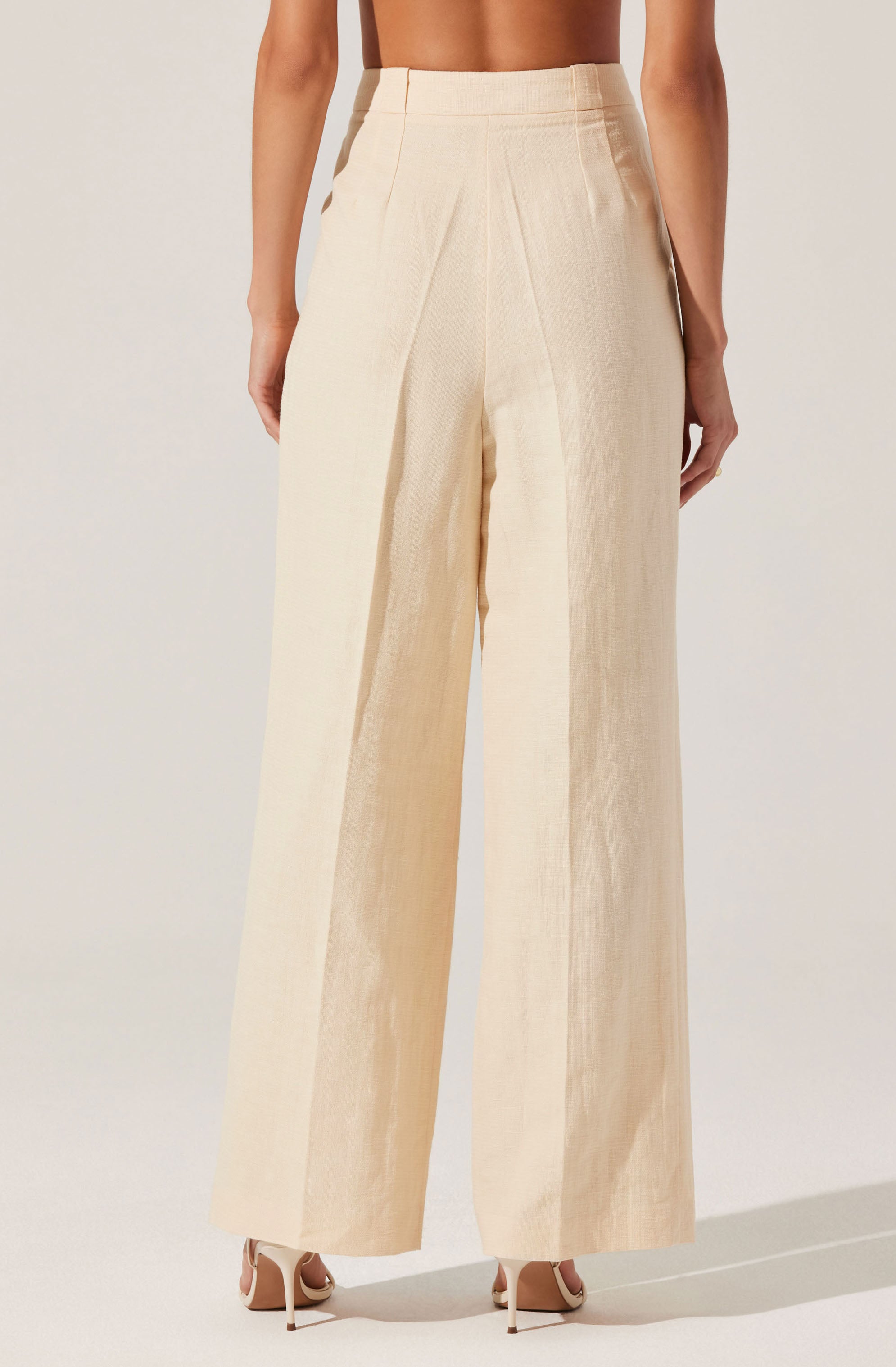 A person is wearing high-waisted, wide-leg pants in a light beige or cream color made from a textured, lightweight fabric. The pants have a clean, tailored appearance with vertical seams running down the legs, and a wide waistband that sits above the hips.