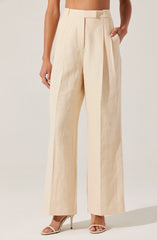 A person is wearing high-waisted, wide-leg trousers in a light beige or cream color, made from a textured fabric. The trousers have a pleat detail at the front and side pockets. The person is also wearing high-heeled shoes with thin straps.