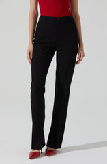 A person is wearing high-waisted black dress pants with a straight-leg cut, secured with a button and zipper at the waist. They are also wearing a sleeveless red top tucked into the pants. The outfit is paired with red pointed-toe high heels.