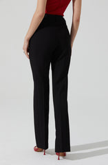 A person is wearing black tailored pants with a high waist and a front creased design. They are also wearing a sleeveless red top. The pants have a classic, straight-leg fit and are paired with red high-heeled shoes.