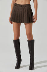 A person is wearing a high-waisted, pleated skirt with a checkered pattern in shades of brown and black. They are also wearing tall black leather knee-high boots. The outfit appears to be styled in a modern, stylish manner.