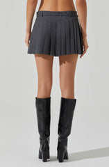 A woman is wearing a high-waisted, dark gray pleated mini skirt and black knee-high leather boots with high heels.