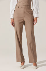 A person is wearing high-waisted, wide-leg tan dress pants with belt loops, paired with a white blouse that has long sleeves with cuffs. The outfit is completed with white pointed-toe shoes.