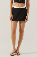 A person is wearing a black cropped top with a single button and a black mini skirt with a white waistband and a single button detail. They are also wearing black strappy high-heeled sandals.