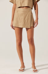 A person is wearing a beige cropped short-sleeve top and a matching beige wrap-style skirt with a single button closure, paired with white open-toe sandals.
