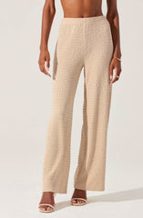 A person is wearing wide-leg beige pants with a textured, woven pattern. The pants have an elastic waistband and a relaxed fit that extends down to the floor, covering the shoes. The individual accessorized with a gold bracelet and gold rings.