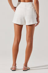 The image shows a woman wearing high-waisted, white shorts made of a lightweight, woven fabric. The shorts have a relaxed fit with a slightly flared hem, and they appear to have side seam pockets. She is also wearing flat, open-toe sandals with ankle straps.