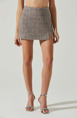 The image features a person wearing a high-waisted, textured skirt with a color pattern of beige and light blue. The skirt has a small slit on the side. They are also wearing silver high-heeled sandals with ankle straps and decorative bows on the toes. The person has rings on their fingers.