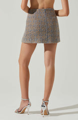 A woman is wearing a high-waisted, textured skirt with a pattern of blue and brown colors. She is also wearing a pair of shiny silver high-heeled sandals with ankle straps.