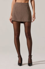 A person is wearing a high-waisted, brown plaid mini skirt paired with sheer black tights and black pointed-toe high heels with ankle straps.