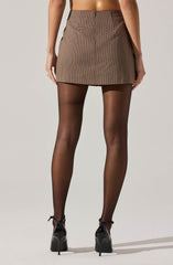The image shows a person wearing a high-waisted, brown houndstooth patterned mini skirt. The person is also wearing sheer black tights and black high-heeled shoes with ankle straps.
