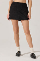 A person is wearing a black mini skirt with a fitted waistband, featuring small horizontal slit pockets on the back. They are also wearing white socks and black loafers with a decorative fringe detail on the top.