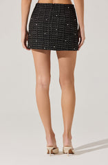 A person is wearing a high-waisted, black mini skirt with a textured, checkered pattern featuring small, shiny embellishments. They are also wearing light-colored high heels.