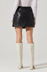 The person is wearing a knee-length black leather skirt with a smooth finish and a high waist. They are also dressed in a long-sleeved, light-colored top and tall, white thigh-high boots with chunky heels.
