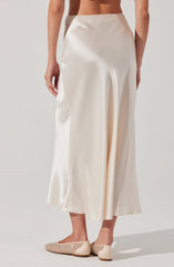 A person is wearing a high-waisted, full-length cream satin skirt with a smooth, shiny finish. They are also wearing beige flats with a decorative pattern of small, shiny embellishments.