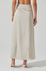 A long, elegant cream-colored satin skirt with a high waist and a smooth, flowing silhouette. The skirt features a subtle slit at the back and is paired with cream high-heeled shoes. The model's top is not visible, but her arms and hands are seen resting at her sides.