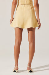 A woman wearing a light yellow textured crop top and matching high-waisted, flared shorts. She is also wearing beige high-heeled shoes.