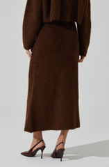 A person is wearing a long, brown, fuzzy skirt that reaches the ankles. They are also dressed in a matching brown, fuzzy top with long sleeves. The outfit appears cozy and warm, with the top slightly loose-fitting. The person is wearing brown high-heeled shoes with pointed toes and ankle straps.