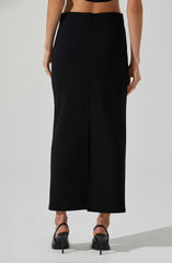 A woman is wearing a high-waisted, wide-leg black skirt that extends to her ankles. She has paired it with black high-heeled shoes with ankle straps. The skirt has a central front slit and is made of a smooth, slightly shiny fabric.