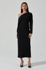 A woman is wearing a black, asymmetric, one-shoulder dress with long sleeves. She has accessorized with gold earrings, a gold necklace, and black pointed-toe heels.
