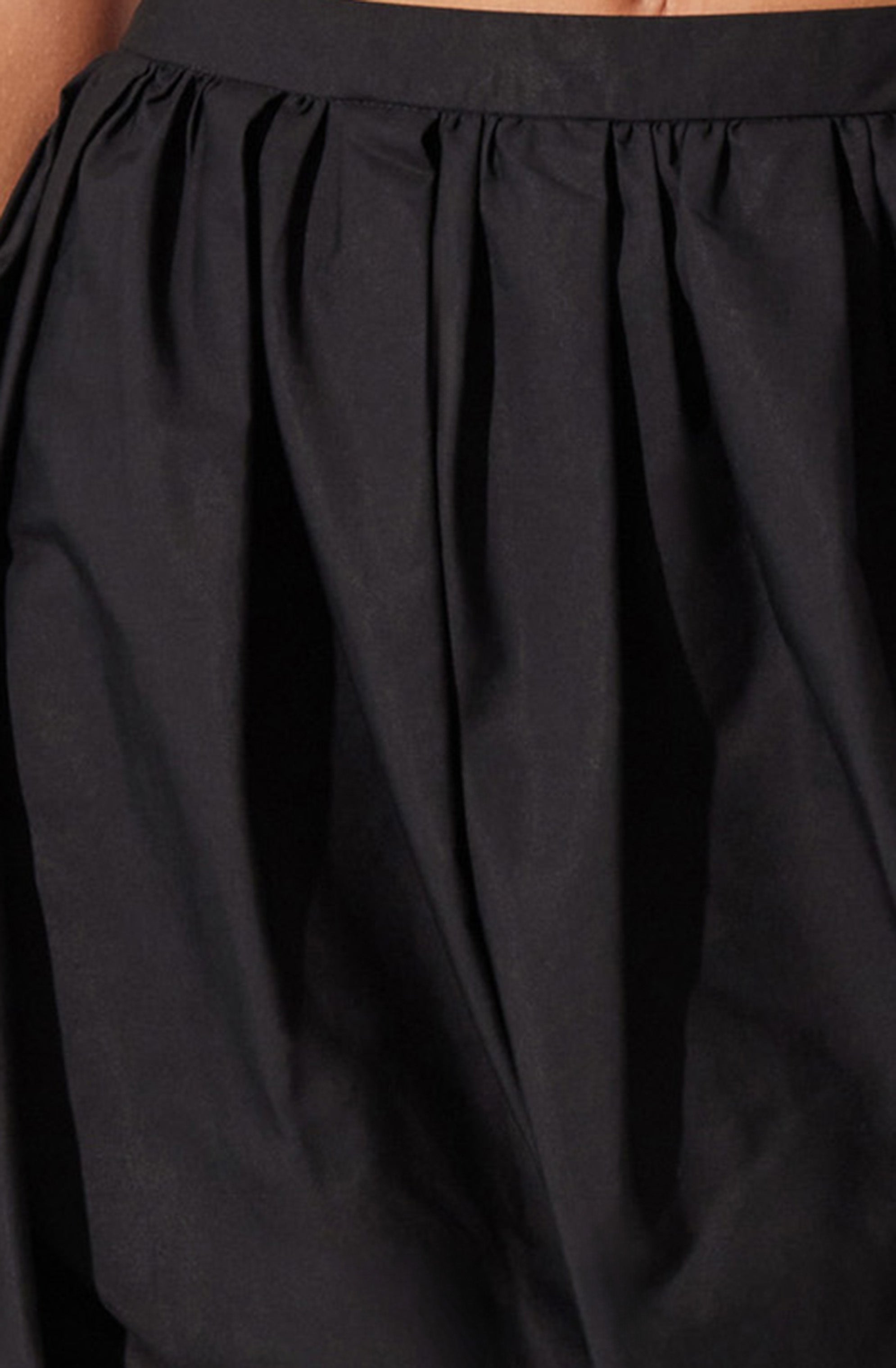 A close-up of a black skirt made from a shiny, smooth fabric. The skirt features a fitted waistband and gathers or pleats starting from the waistband, creating a voluminous, flowing appearance.