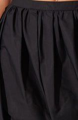 A close-up of a black skirt made from a shiny, smooth fabric. The skirt features a fitted waistband and gathers or pleats starting from the waistband, creating a voluminous, flowing appearance.