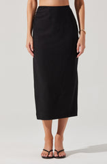 A woman is wearing a high-waisted, ankle-length black skirt made of a smooth, possibly satin-like fabric. She has paired it with black strappy sandals and a gold bracelet on her right wrist. The image focuses on her lower body from the waist down.