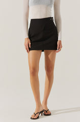 A woman is wearing a fitted, long-sleeved, ribbed sweater with a gradient color pattern that transitions from light to dark. She has on a high-waisted, black mini skirt with a side buckle detail. She is also wearing strappy, black high-heeled sandals.