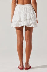 A woman is wearing a white, tiered, ruffled skirt with an elastic waistband. She is also wearing red flip-flops.