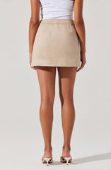 The image shows a person wearing a beige mini skirt with a straight cut and a waistband. They are also wearing a white sleeveless top tucked into the skirt. The person has light brown skin and is wearing beige high-heeled shoes.