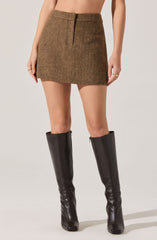 A woman is wearing a high-waisted, brown tweed mini skirt with a subtle herringbone pattern. She pairs it with tall, black leather knee-high boots.